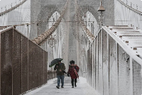 People walk across the Brooklyn Bridge as snow falls during a winter storm in NYC, Feb 22, 2026