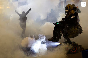 A person gestures amid tear gas as law enforcement officers advance to disperse demonstrators