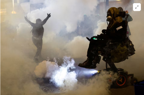 A person gestures amid tear gas as law enforcement officers advance to disperse demonstrators