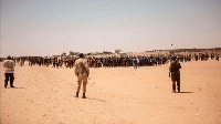 Nigerien soldiers stand guard as a crowd of migrants gather in Assamaka