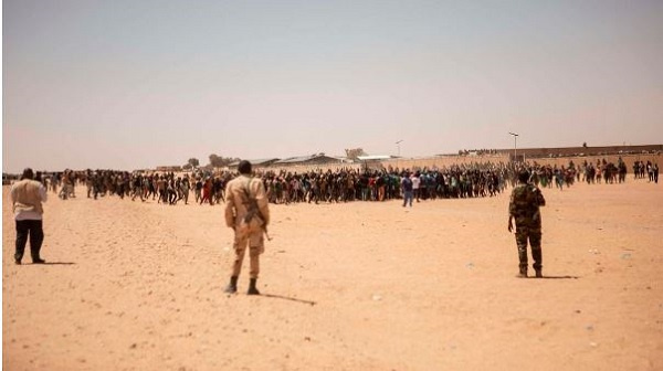 Nigerien soldiers stand guard as a crowd of migrants gather in Assamaka