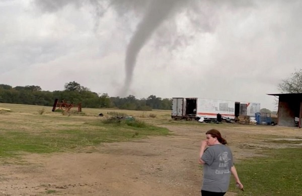 A woman walks on a farm as the funnel cloud of a tornado is seen in the background in Greenview