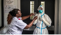 A nurse is assisted by a colleague in donning personal protective equipment at an isolation facility