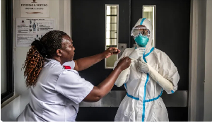 A nurse is assisted by a colleague in donning personal protective equipment at an isolation facility