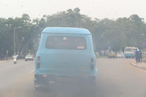 A rickety commercial car in Ghana moving freely with thick exhaust fumes.
