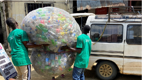 Employees load a sack of plastic bottles onto a bus after collection from a dump site