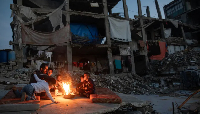 Displaced Palestinians warm themselves near a fire among the ruins of their destroyed home