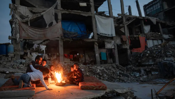 Displaced Palestinians warm themselves near a fire among the ruins of their destroyed home