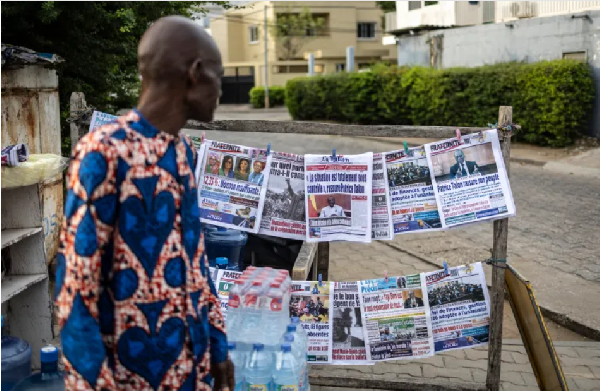 A vendor looks at newspapers displayed on a stall, on Dec. 8, 2025, a day after the failed coup