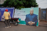 A motorcyclist stands beside a billboard featuring presidential candidate Paul Hounkpe in Cotonou