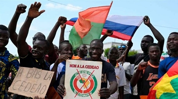 A small group of protesters hold Russian and Burkina Faso flags as they protest against Ecowas