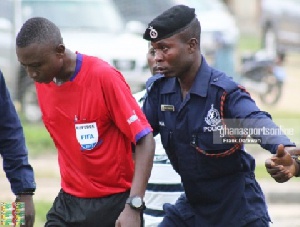 A Ghanaian referee being escorted out of the field after a match