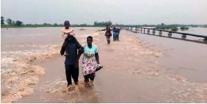 Residents wade across a flooded road in Butaleja District