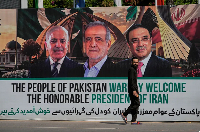 A man passes a billboard of Pezeshkian, Zardari, and Sharif in Islamabad