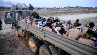 Israeli soldiers stand beside a truck in Gaza transporting Palestinian detainees, including a woman