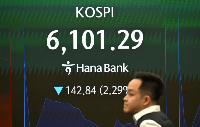 A currency dealer walks past an electronic screen showing South Korea's benchmark stock index