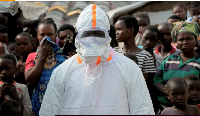 A health worker stands near displaced people waiting for the burial of suspected ebola victims