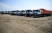 People stand near trucks loaded with aid in Port Sudan during the launch of humanitarian aid convoy