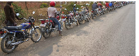 Motorcycle taxi riders queue along the road for customers