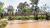 People walk over a water bridge after their homes were swamped following rains
